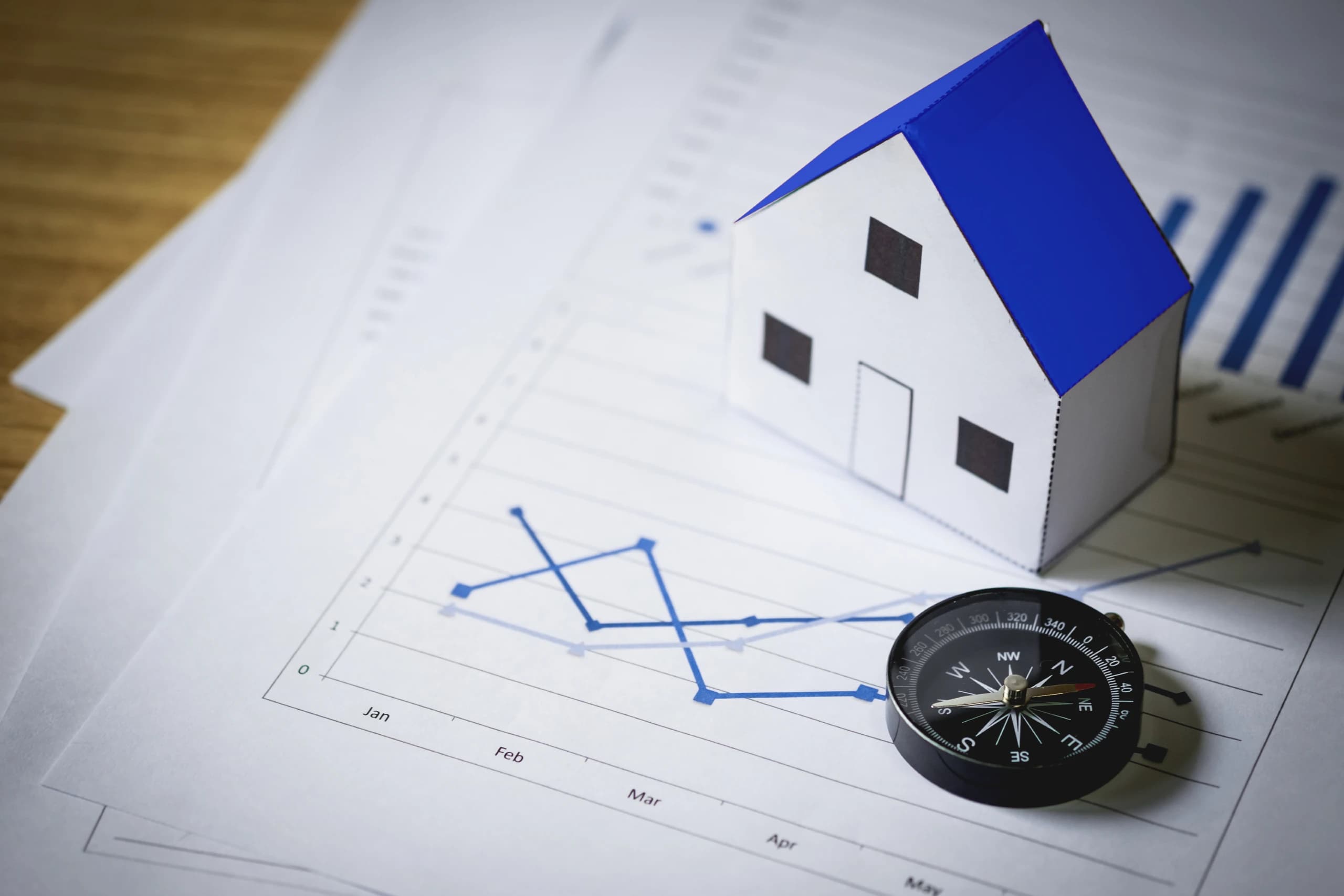 home on top of paper with charts on it and a compass next to the house